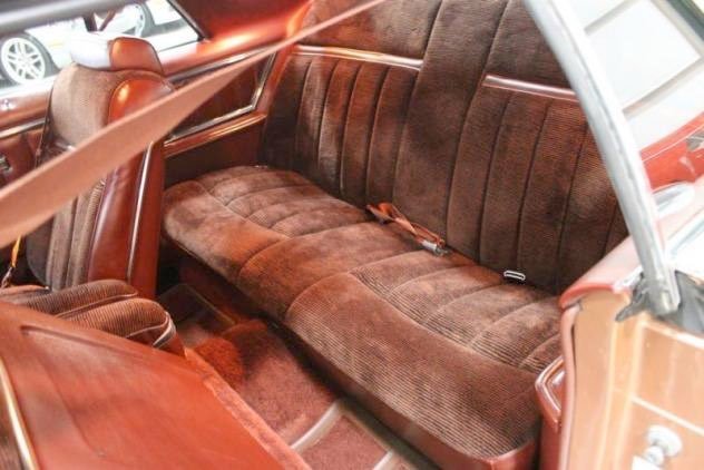 The interior of a vintage car showcasing a brown fabric bench seat and matching upholstery.
