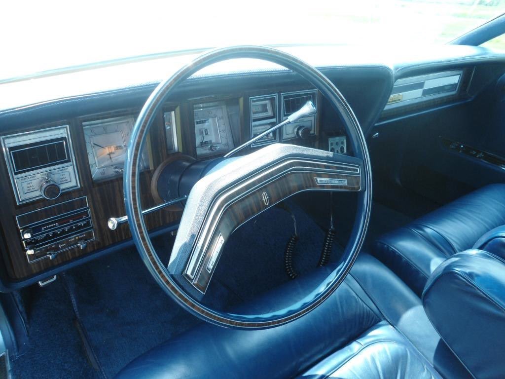Interior of a vintage car with a wood-paneled dashboard, large steering wheel, and blue leather seats.