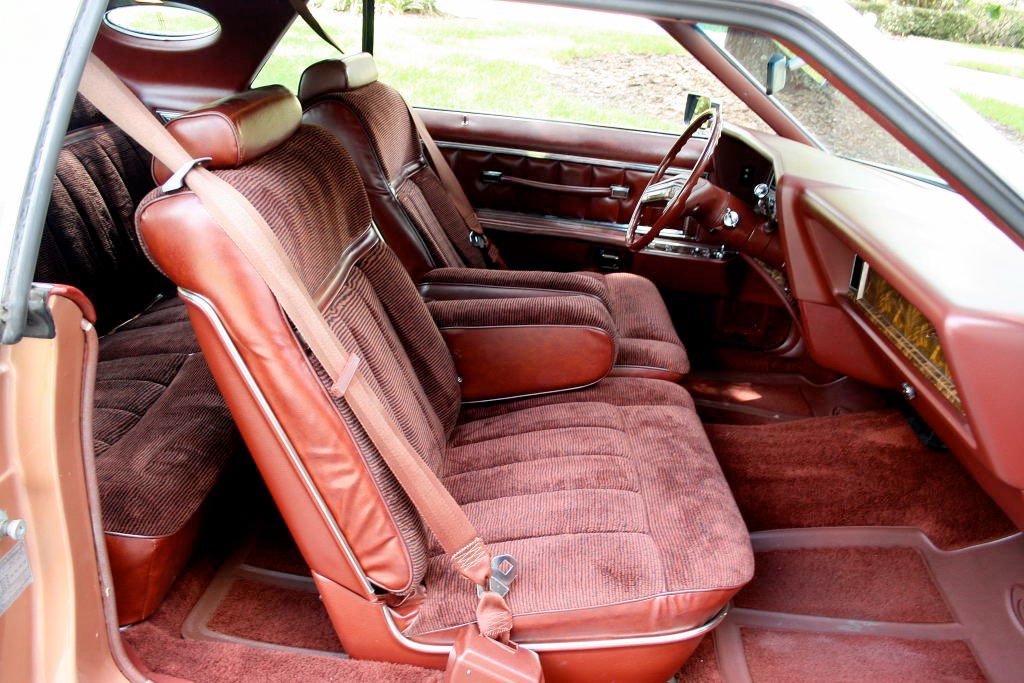 Interior of a vintage car showing burgundy cloth and leather seats, dashboard, and steering wheel.
