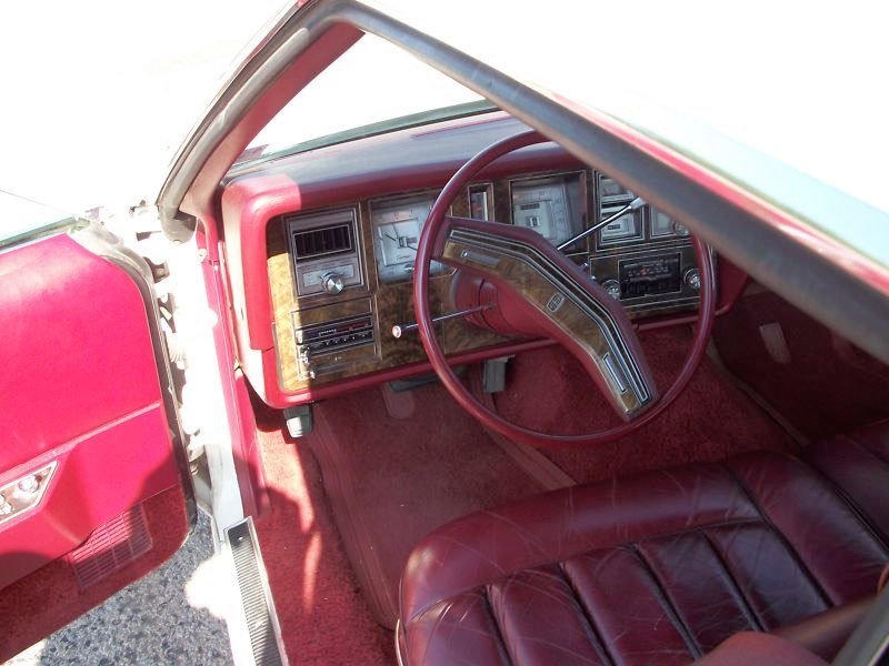 Interior of a vintage car with a red dashboard, steering wheel, and leather seats.