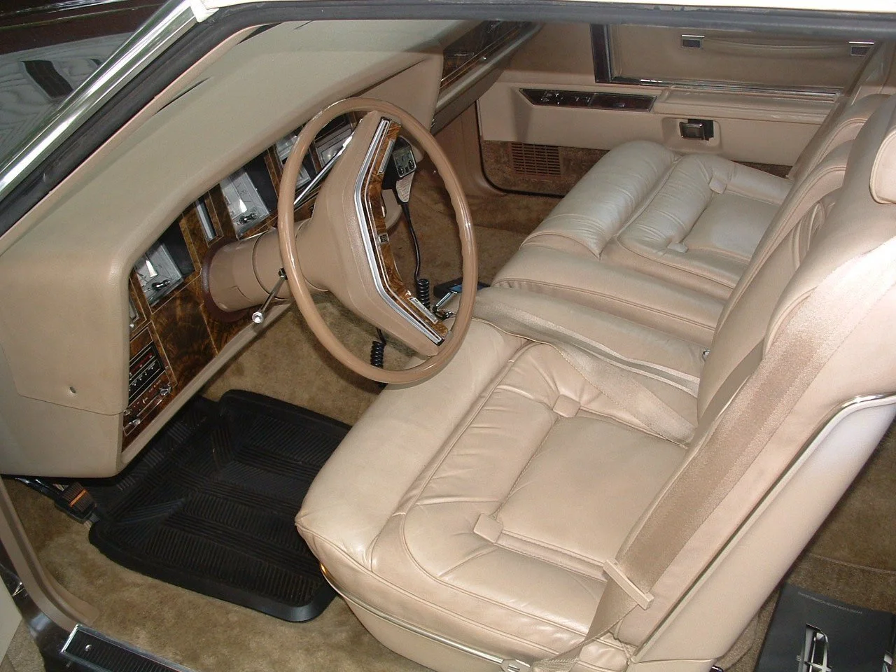 Interior of a vintage car showing beige leather seats, wooden dashboard trim, and a steering wheel.