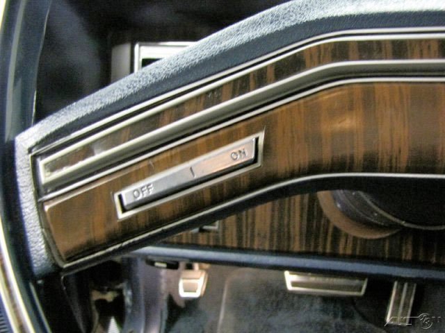 Close-up of a vintage car's dashboard with a wood grain finish and an on/off switch.