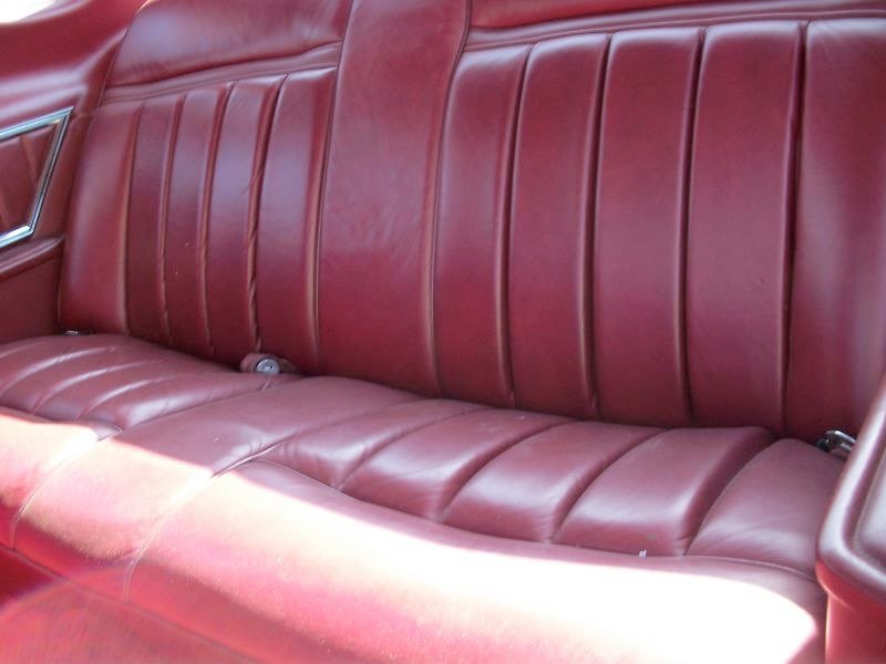 Red leather car backseat with vertical stitching.