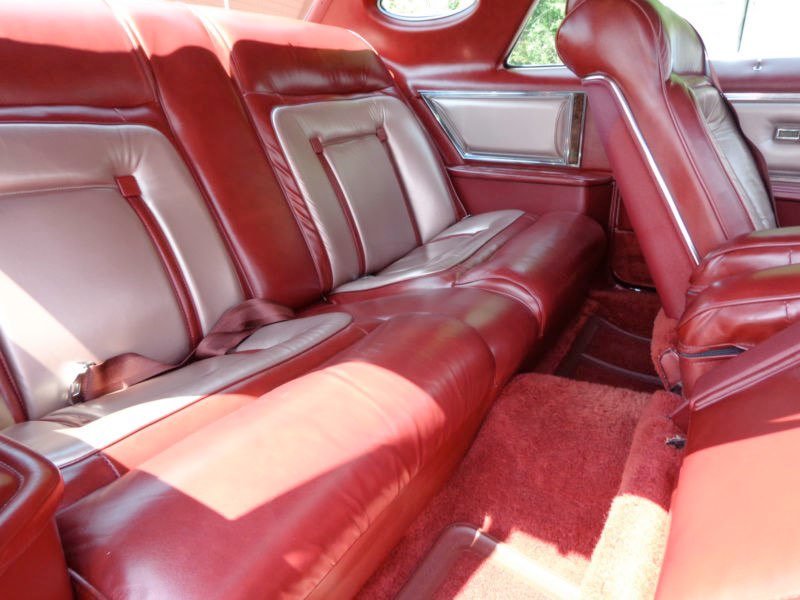 Interior of a vintage car with red and beige leather seats and red carpeting.