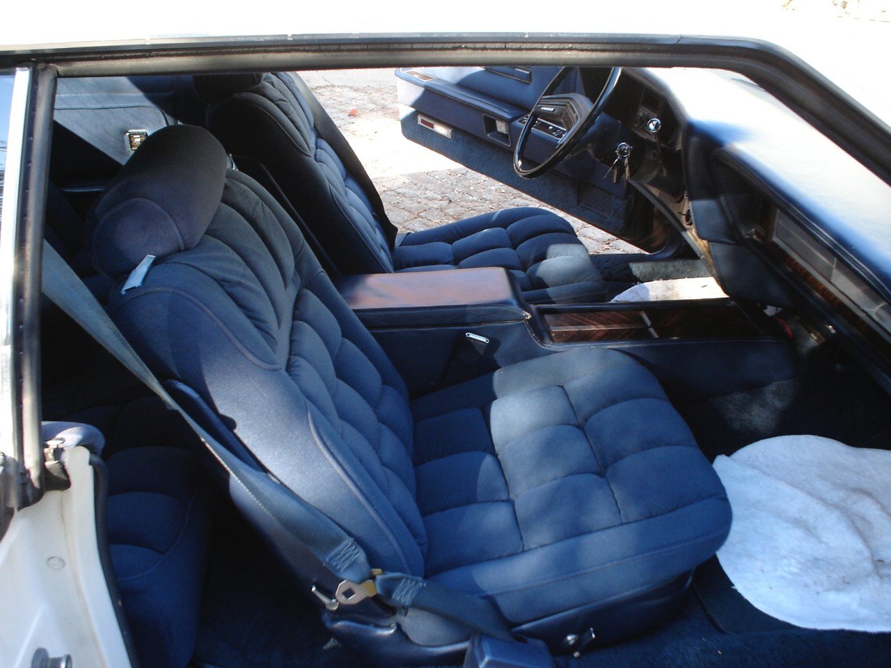 Interior of a vintage car showing navy blue plush front seats, dashboard, steering wheel, and a white cloth on the floor.