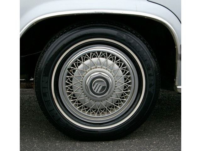 Close-up of a vintage car wheel with a wire-spoke hubcap and a radial tire.