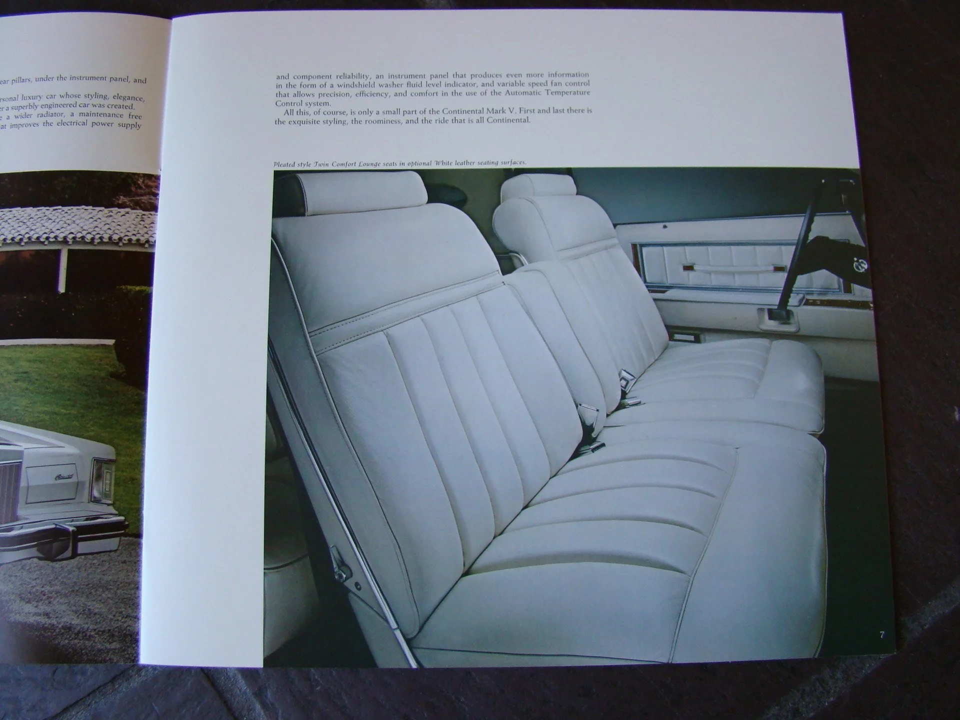 Inside view of a vintage car showing white leather bench seats with headrests and seat belts.