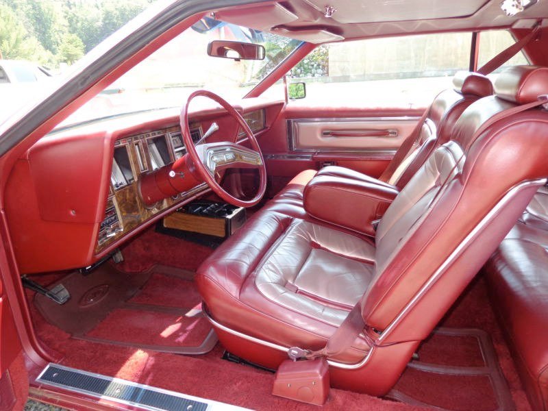 Interior of a vintage red car with leather seats, wood panel dashboard, and steering wheel.