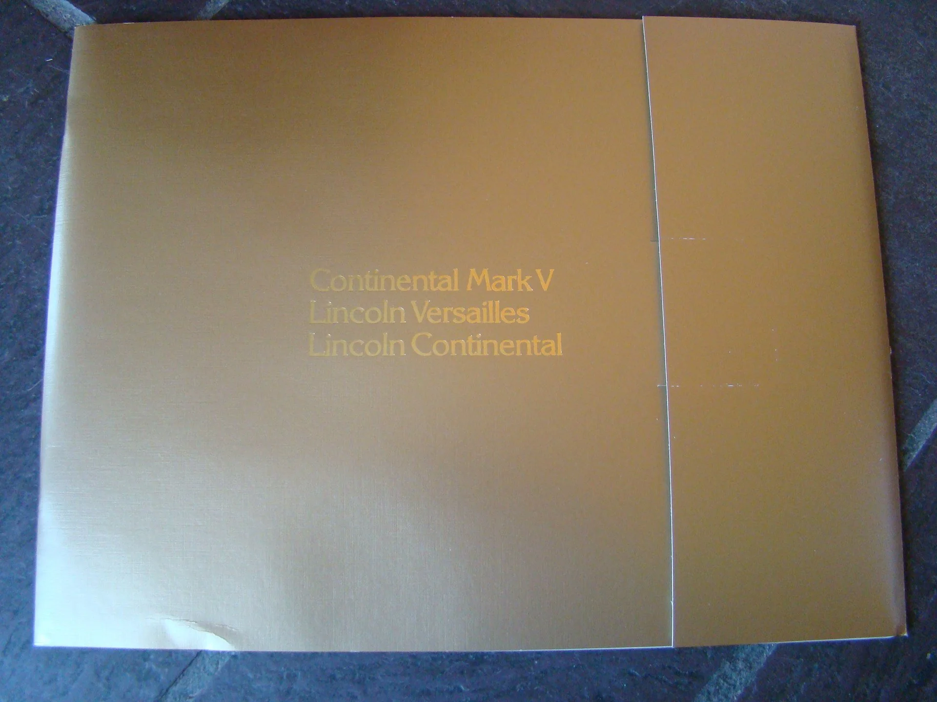 A gold-colored box with text that reads 'Continental Mark V, Lincoln Versailles, Lincoln Continental' in gold lettering.
