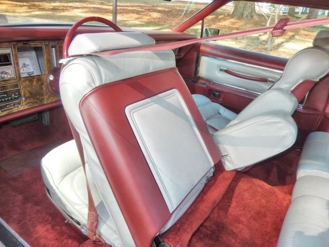Interior of a vintage car with white and red leather seats, wood paneling, and a red carpet floor.