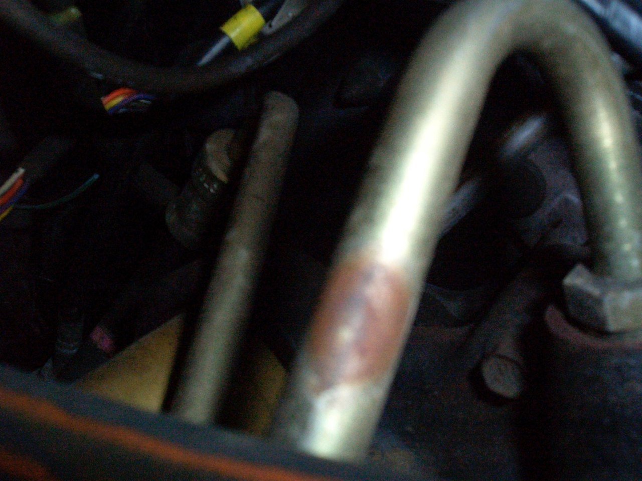 Close-up of a vehicle's engine compartment showing metal pipes and nearby wires.