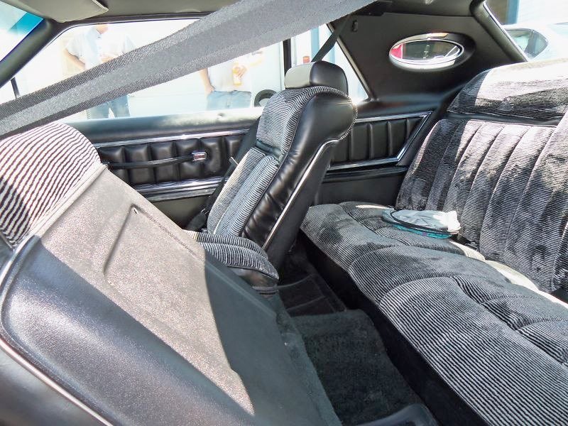 Interior of a vintage car showing bench seats with striped fabric upholstery, black accents, and a sunshade or sun visor attached to the window.