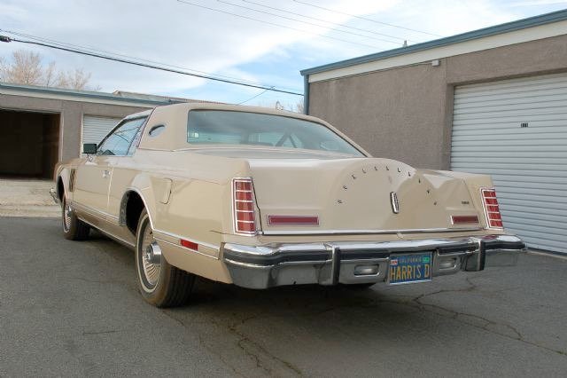 Rear view of a vintage beige Lincoln Continental car parked on a driveway, with house and garage in the background.