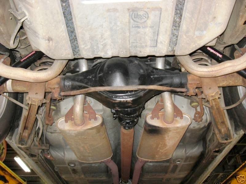 Underneath view of a vehicle's rear differential and exhaust system showing rust on the frame and components.