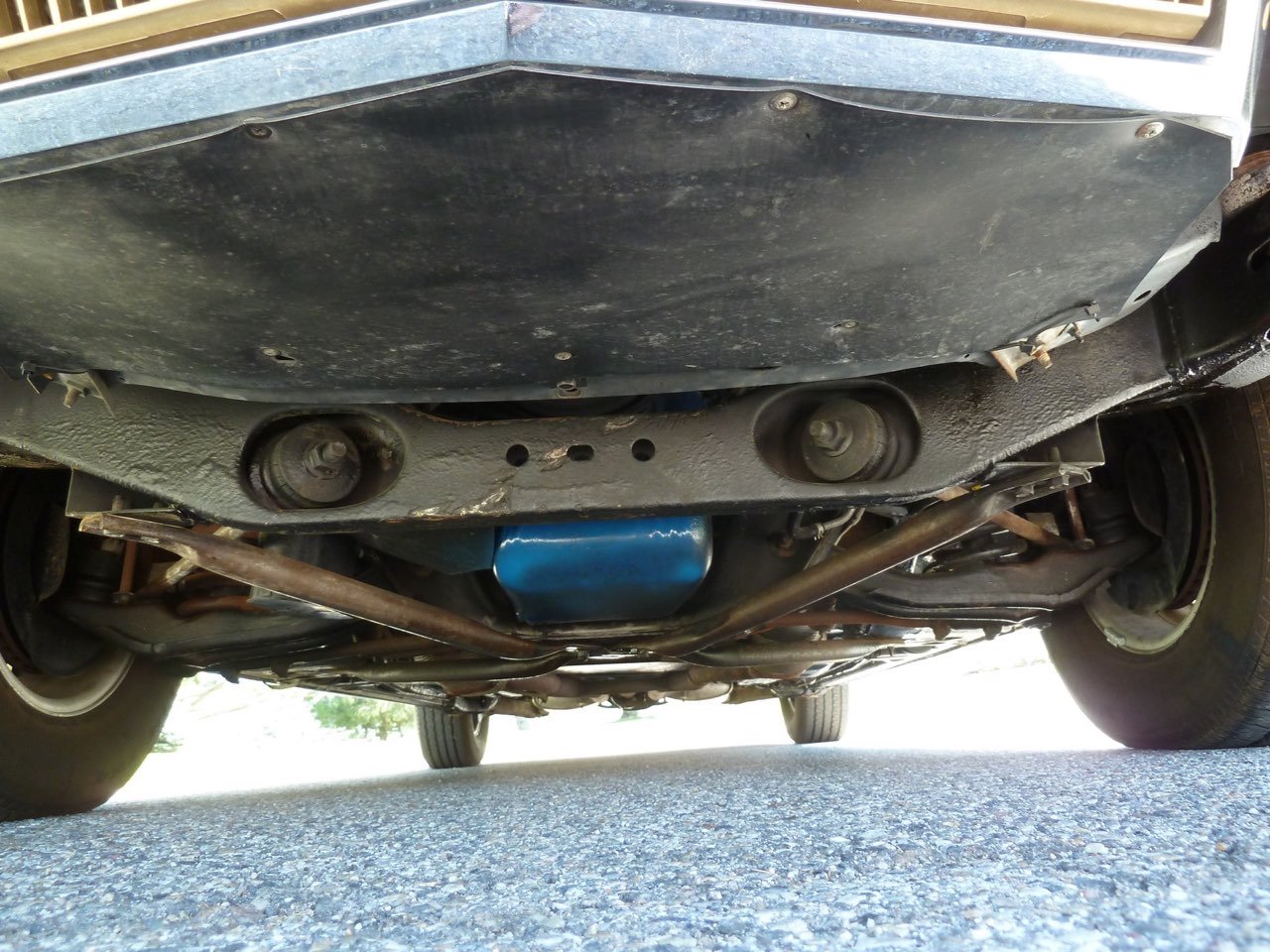 Underside of a car showing suspension and steering components, with a blue oil pan and exhaust pipes visible.