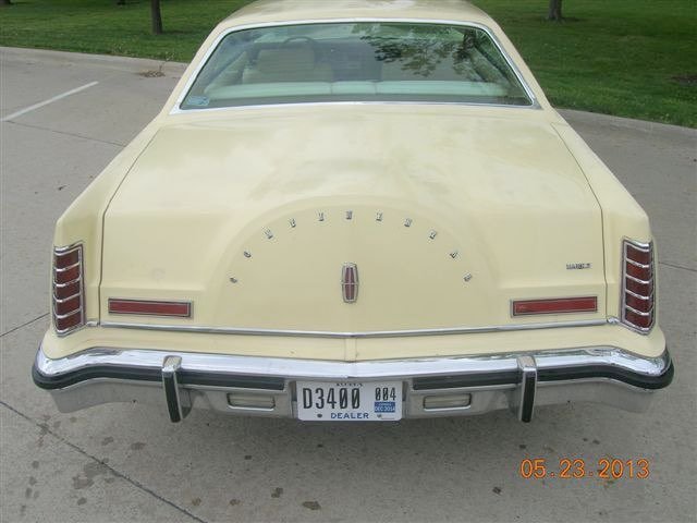 Rear view of a vintage beige Mercury Marquis car with a license plate from Ohio, parked on a concrete driveway with grass and trees in the background.