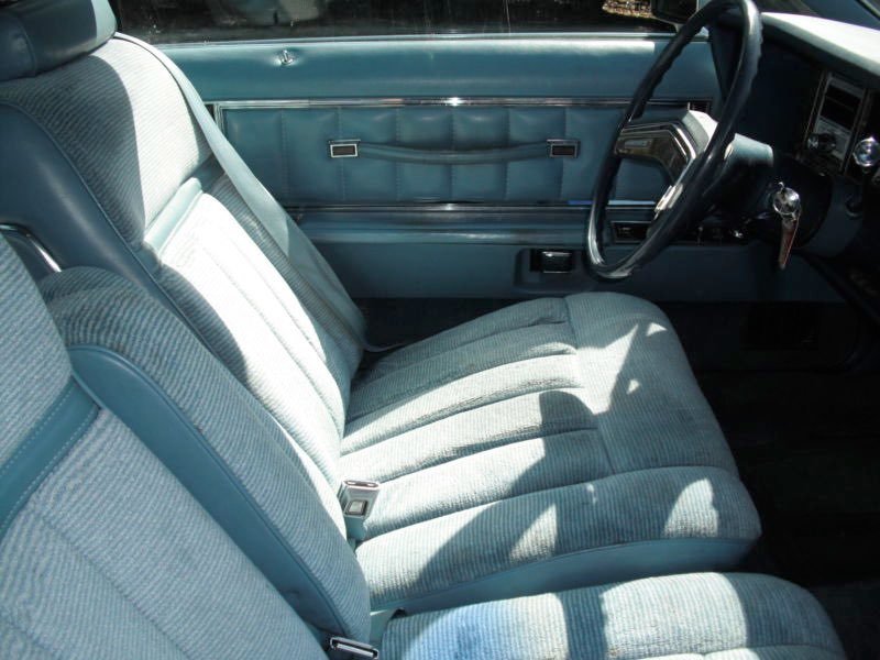 Interior of a vintage vehicle showing a blue cloth bench seat, steering wheel, and door panel with tufted design.