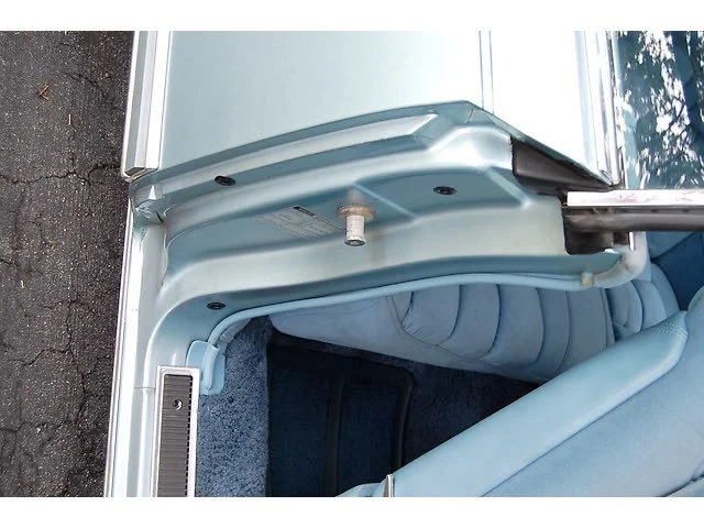 Close-up of vintage car door interior showing light blue upholstery and carpeted floor.