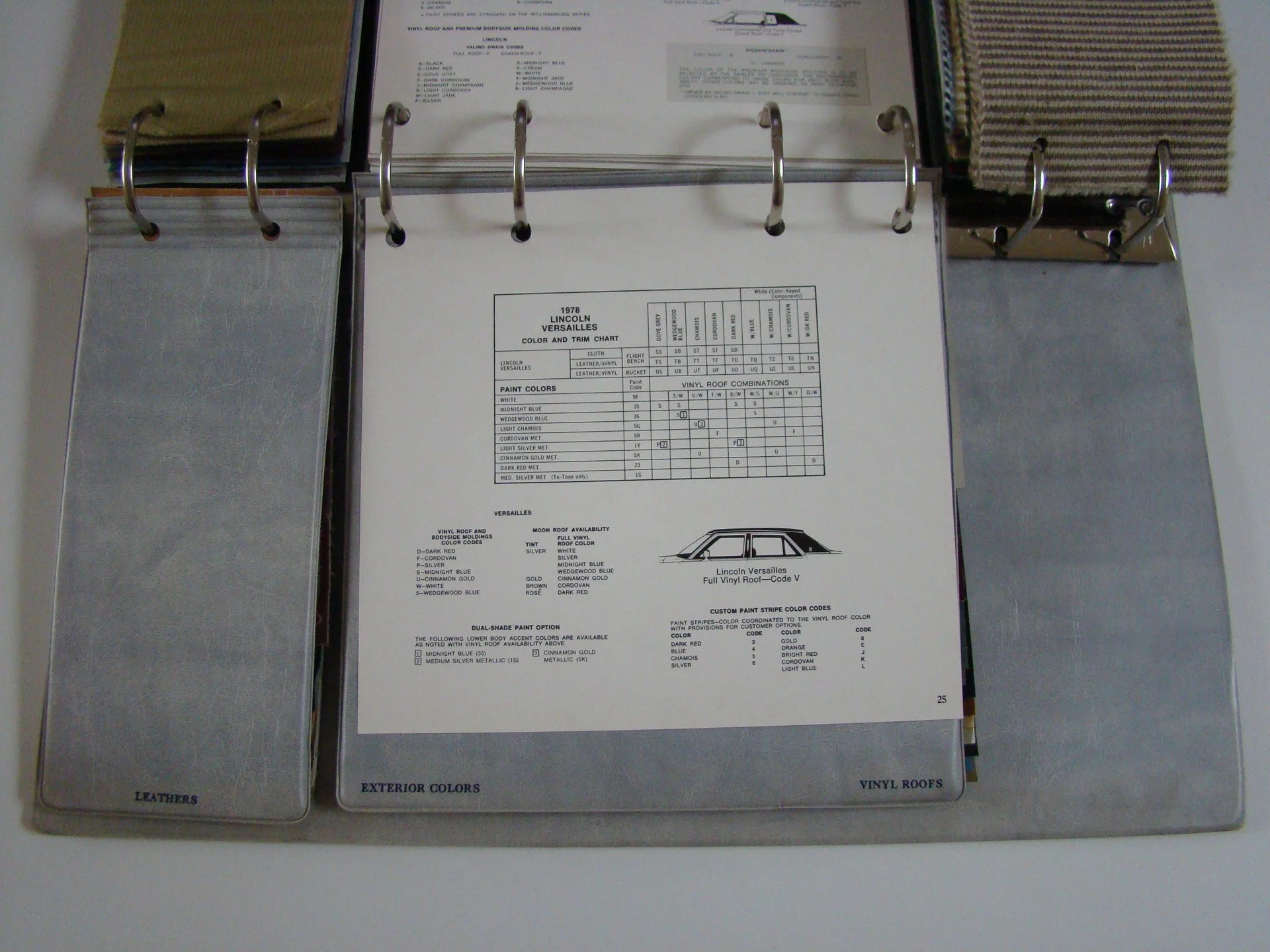 Open binder with pages showing automotive paint and color options for a 1978 Lincoln Versailles, including fabric, vinyl, and exterior paint colors, with sample swatches attached.