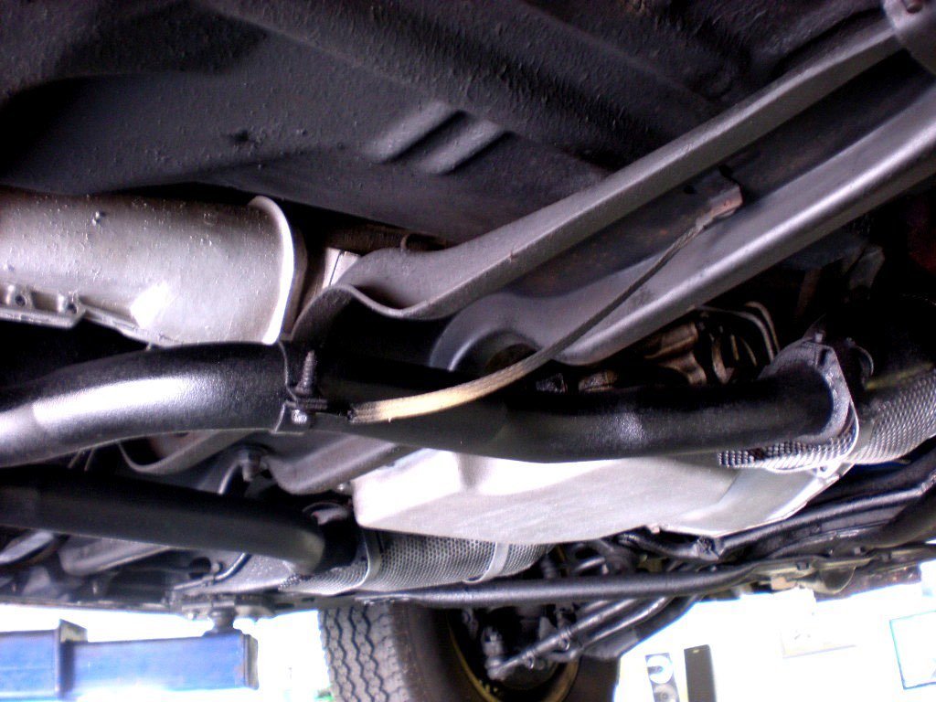 Underneath view of a vehicle's engine and suspension components, including the oil pan, pipes, and parts of the frame.