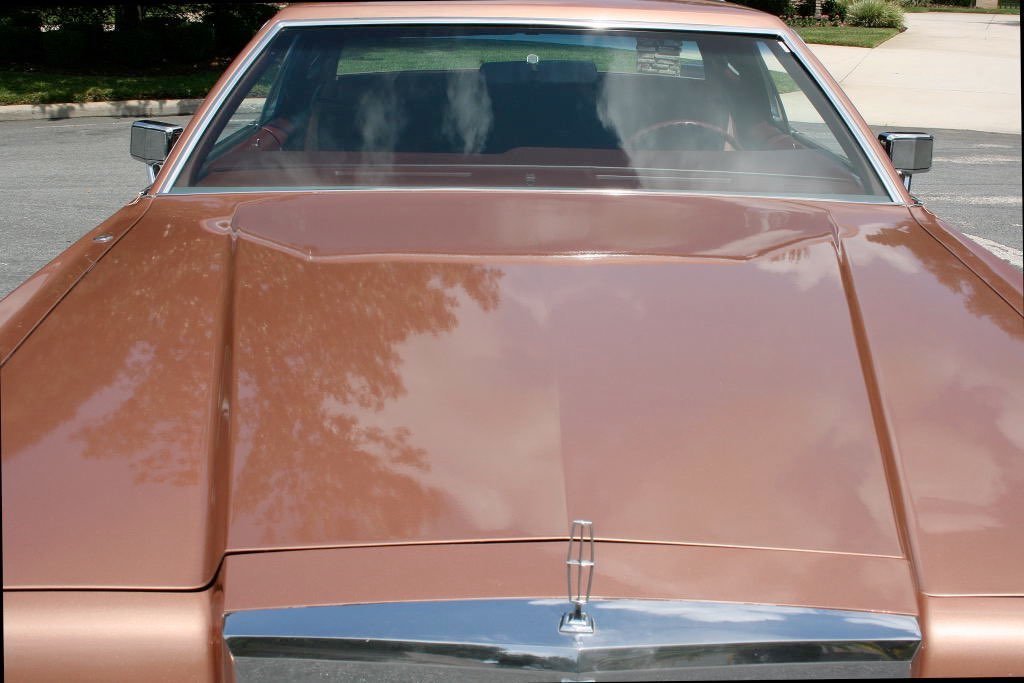 Front view of a vintage orange car parked outdoors, showing the hood, windshield, and side mirrors.