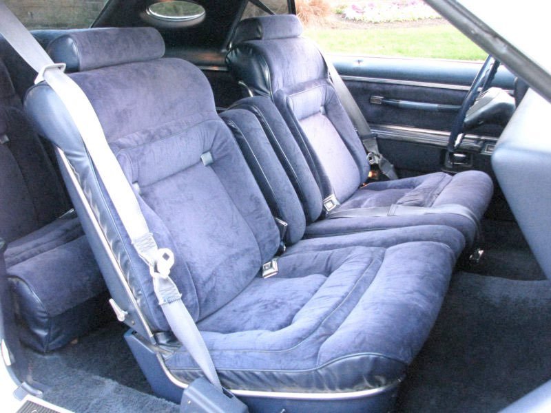 Interior of a car showing the front passenger and driver seats in dark blue velvet upholstery with seat belts, dashboard, and part of the steering wheel.
