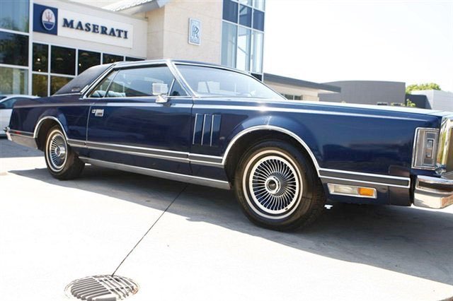A vintage blue car parked outside a Maserati dealership.