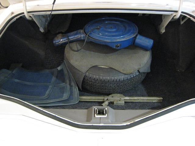 Car trunk containing a blue air compressor, a spare tire, a gray mat, and some plastic containers.