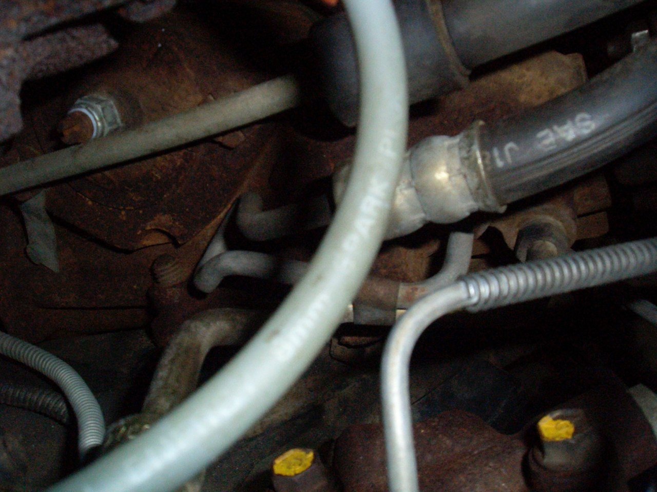 A close-up view of engine hoses and rusted metal components inside a vehicle's engine compartment.