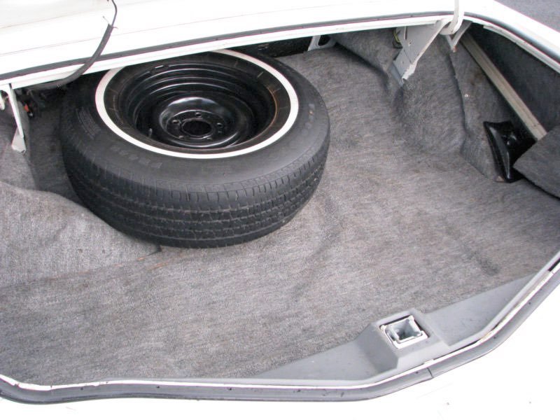Car trunk with a spare tire stored inside on a gray carpeted surface.