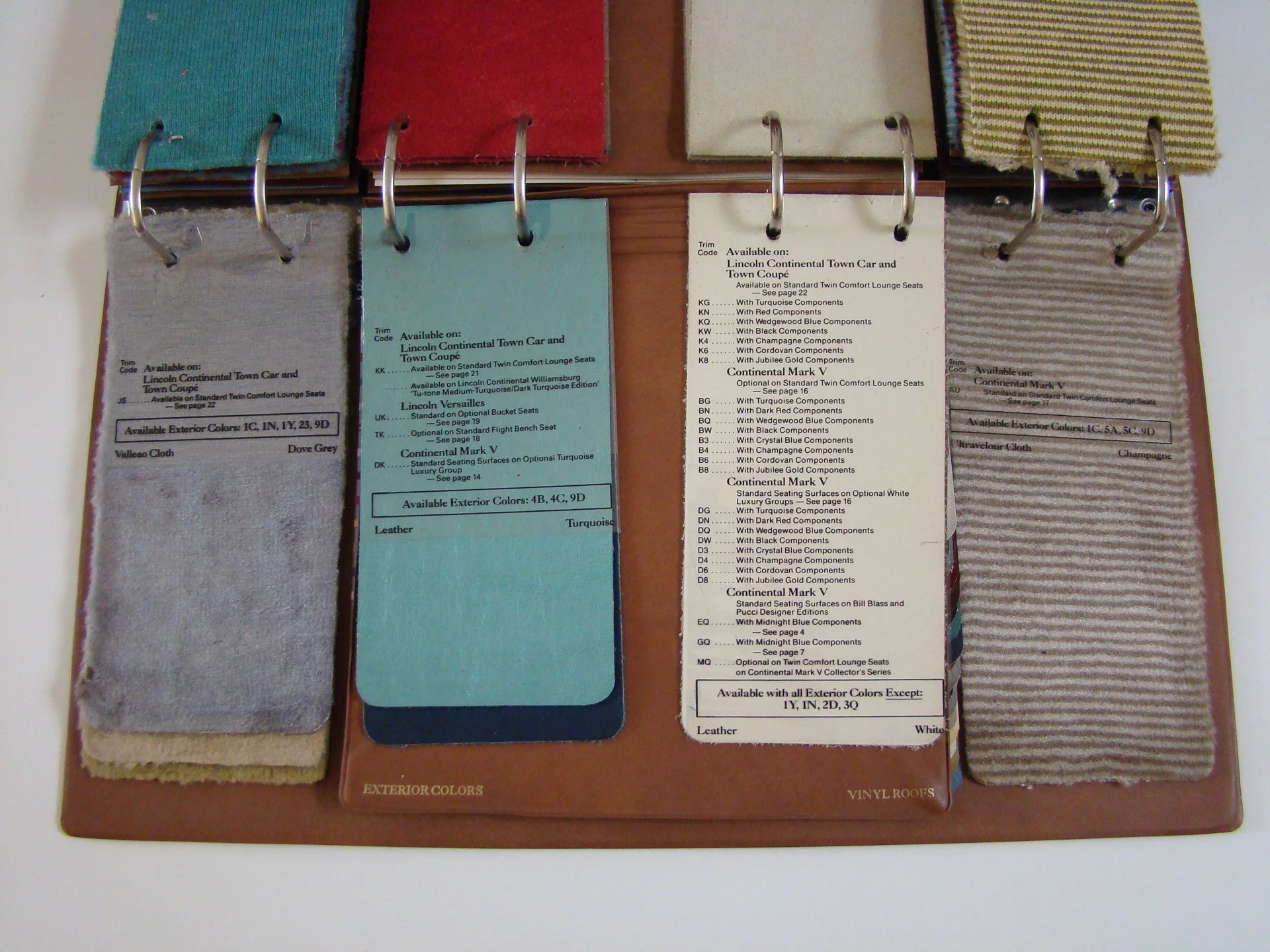Color and material samples, including fabric swatches, laminated color cards with trim codes, and sample labels, laid out on a binder.