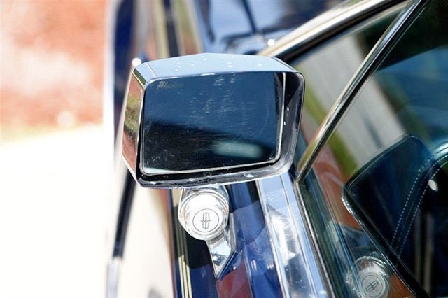 Close-up of a car's side mirror and a small round object attached below it on a blue vehicle.