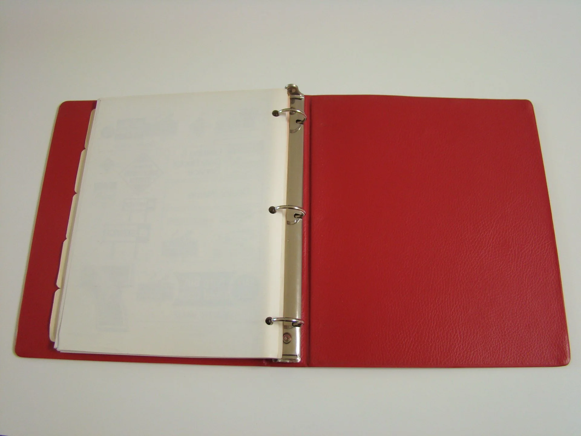 Open red binder with loose leaf paper inside on a white surface.