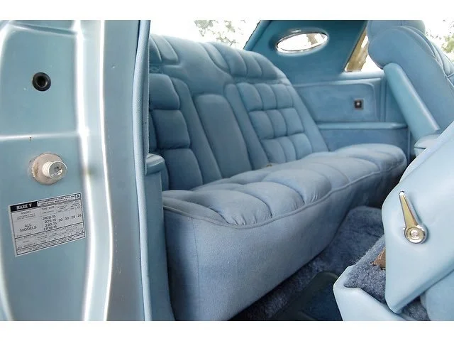 The interior of a vintage car showcasing a plush, light blue upholstered back seat with tufted design and matching side panels.