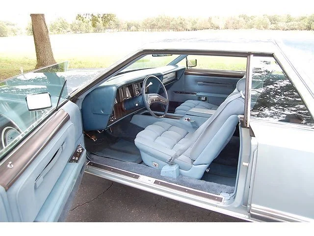 Interior of a vintage blue car showing front seats, dashboard, and steering wheel, with the driver's side door open.