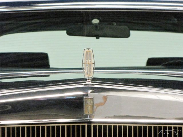 Close-up of the front of a black vintage car showing the chrome hood ornament and grille.