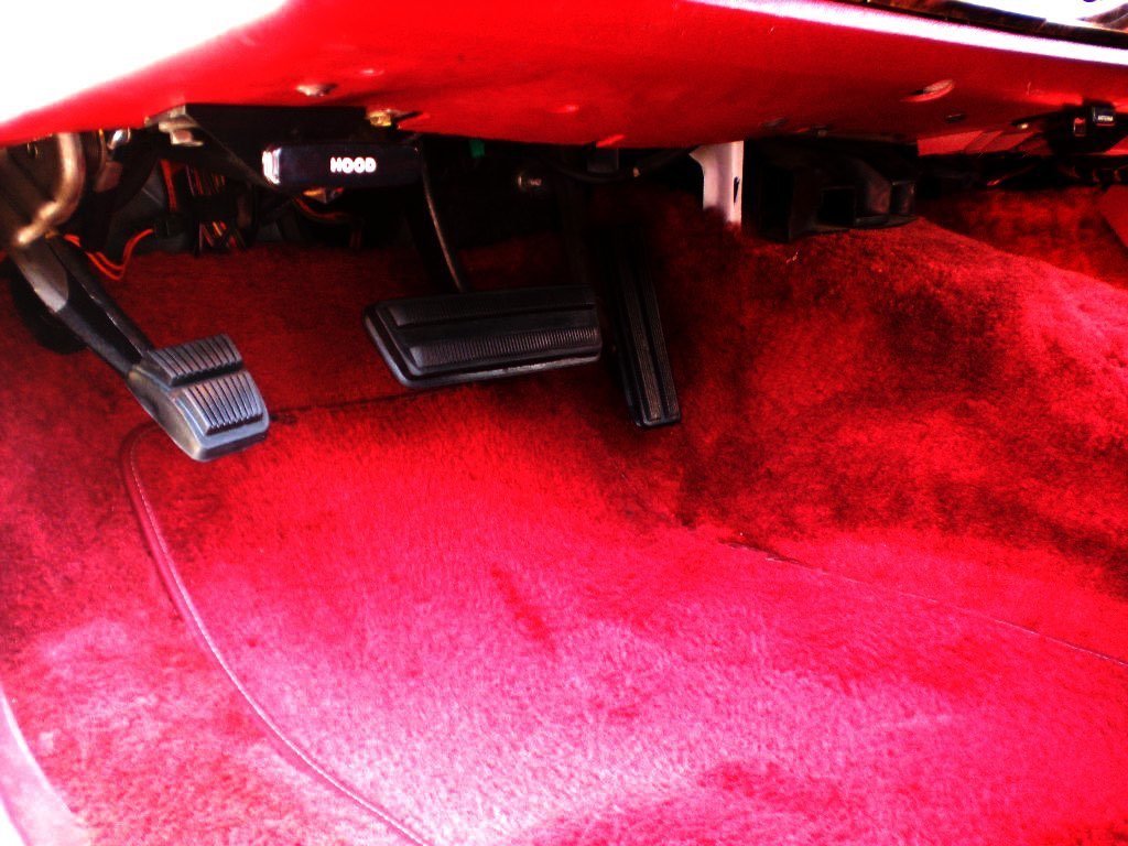 Red car interior floor with accelerator, brake, and clutch pedals.