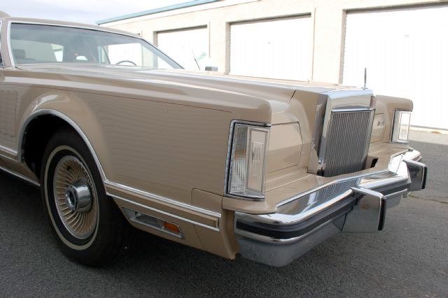 A vintage beige car parked in front of a beige building with garage doors.