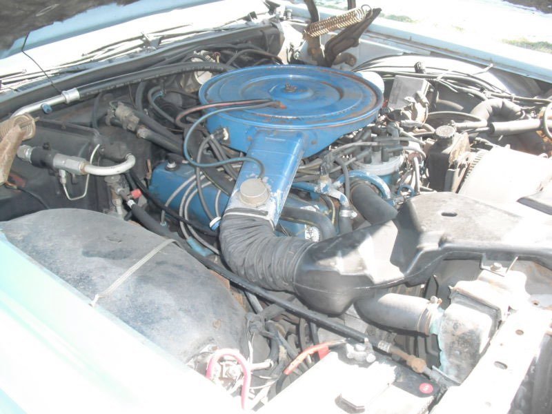 Close-up of an old car engine with a blue air filter cover and various hoses and wiring.