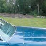 Close-up of a blue car with a cracked windshield, parked on grass near a metal fence.