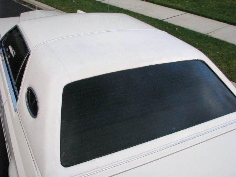 Top view of a white car parked on the street, showing the rear window and part of the roof.