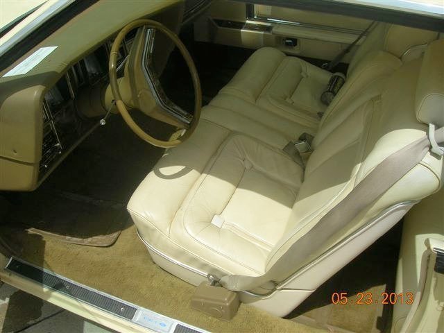 Interior of an old car showing beige leather front seats, steering wheel, and dashboard.