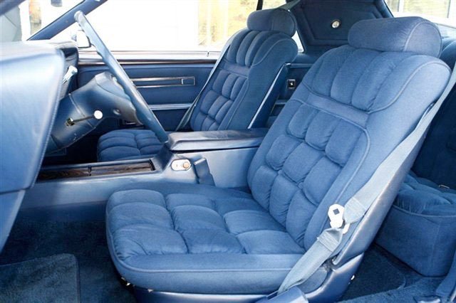 Interior of a vintage car with blue upholstered front and back seats, and a steering wheel.