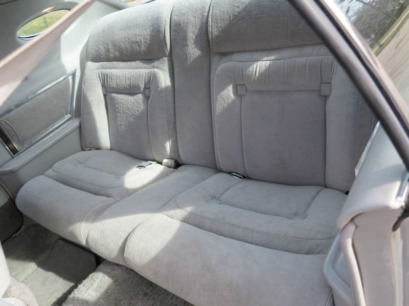 The backseat of a car with light gray fabric upholstery, showing some signs of wear and creases.