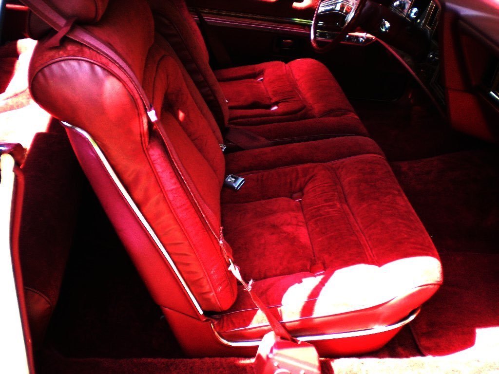 Inside a vintage car with red plush upholstery on the seats and interior panels, showing the front passenger seat and part of the dashboard.