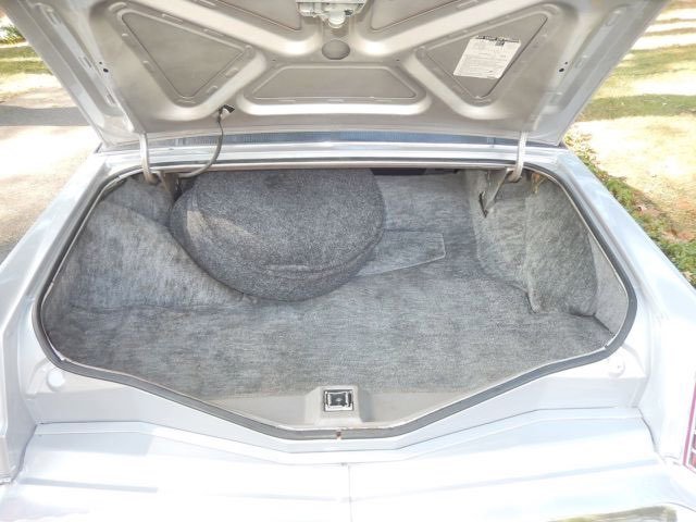 Open car trunk showing gray carpet lining and a spare tire covered with a gray cover.