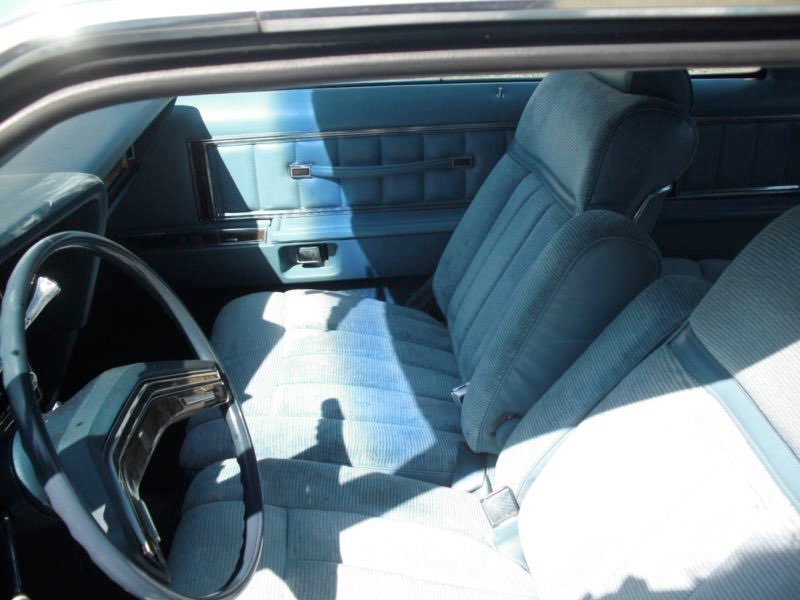 The interior of an older vehicle showing a front bench seat with light blue upholstery and a dashboard with a steering wheel.