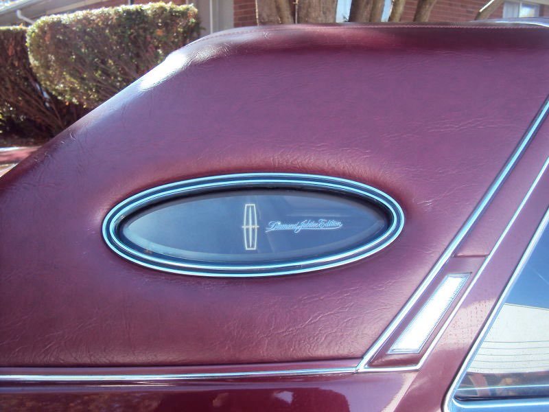 Close-up of a vintage car trunk with a decorative oval emblem that reads "Diamond of the Edition," on a maroon surface.