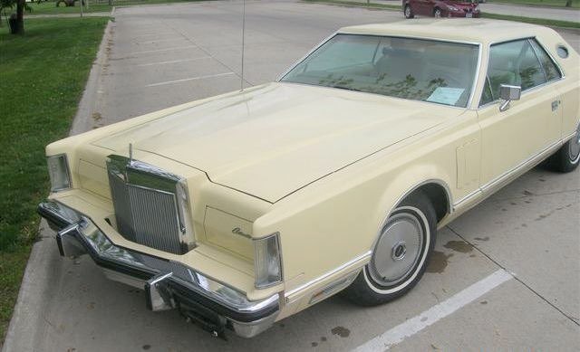 A vintage cream-colored car with a boxy shape and distinctive front grille, parked in a parking lot.