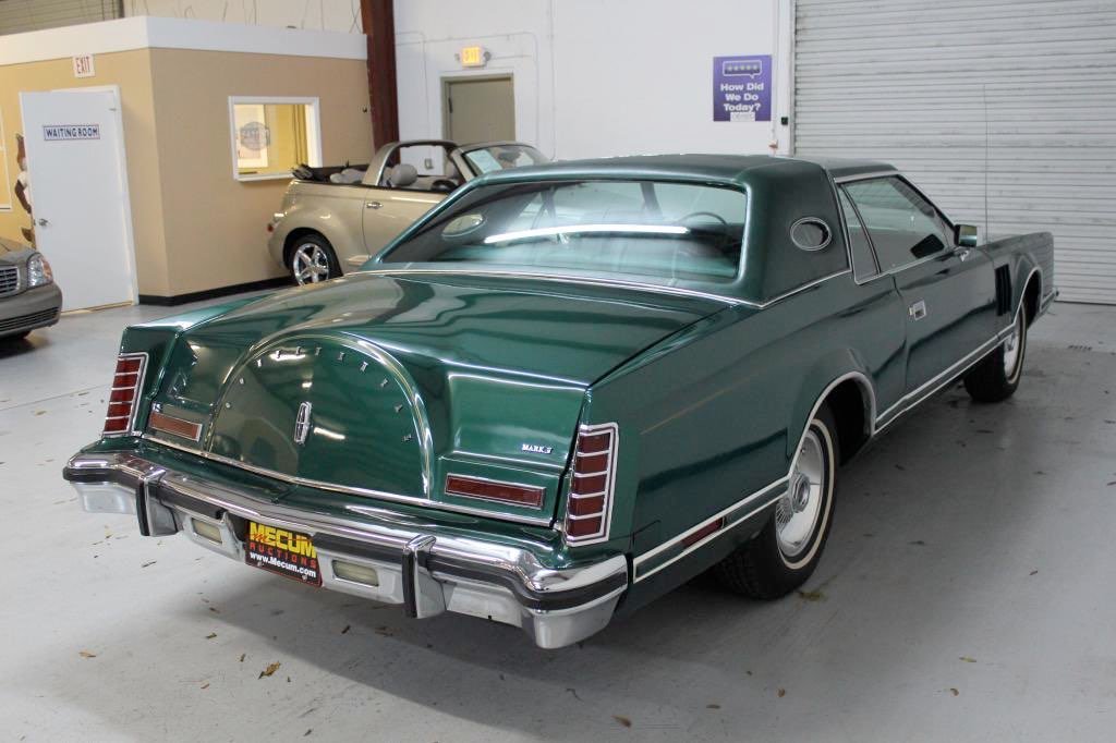 A vintage green Lincoln Mark VI coupe parked indoors, with beige and silver cars visible in the background.